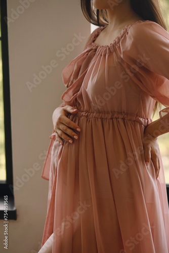 Close up photo of a pregnant belly. Pregnant woman in pink dress holding her hand on belly. Love concept