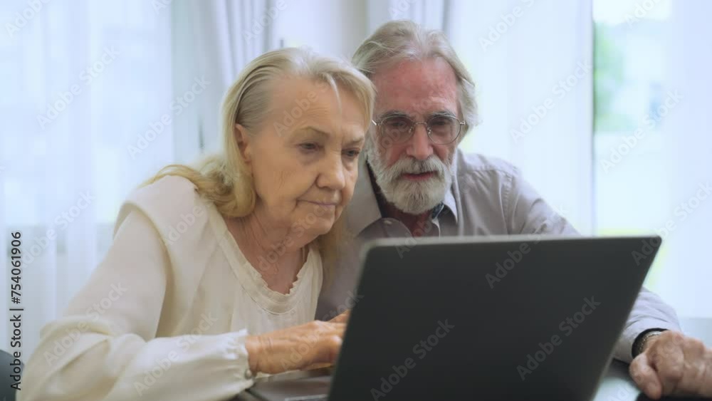 Elderly couple is deeply focused on a laptop screen, engaged in learning or communicating in their home environment. Elderly couple is deeply focused on a laptop screen, engaged in learning or communicating in their home environment.