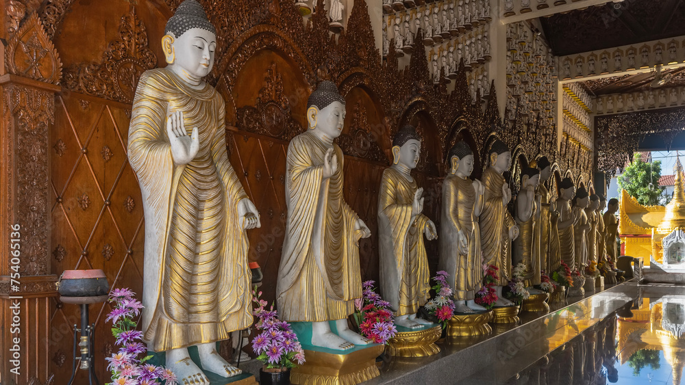 A row of Buddha statues at Burmese Buddhist Temple Dhammikarama. A golden stupa is visible in the opening. A mirror reflection on the floor. Malaysia. Penang.