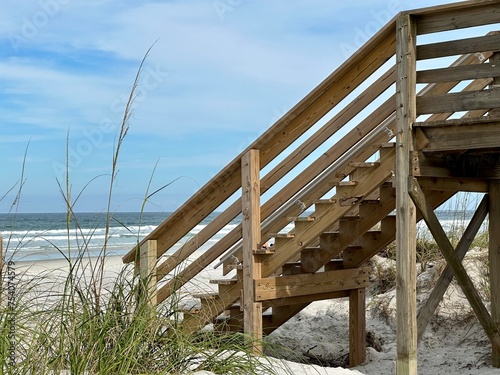 A wooden walkway and stairs lead to the beach, adjacent to the dunes, with sea grass, ocean waves, and the expansive sky at Ponce Inlet, FL.