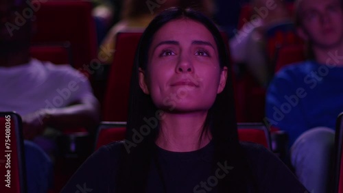 A woman shed tears from watching a film in a cinema, a woman watches the premiere in a cinema and shed tears from a powerful scene, tears appeared in the eyes of a young woman in a cinema.