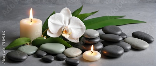Zen stones, candles, and white orchid on green-grey background.
