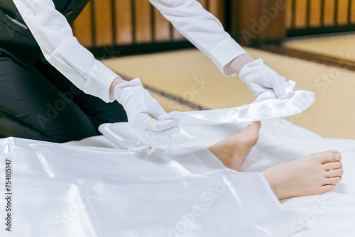 故人の死装束・脚絆をつける湯灌師・納棺師・おくりびと・エンバーマーの日本人女性（エンゼルケア・清拭）
