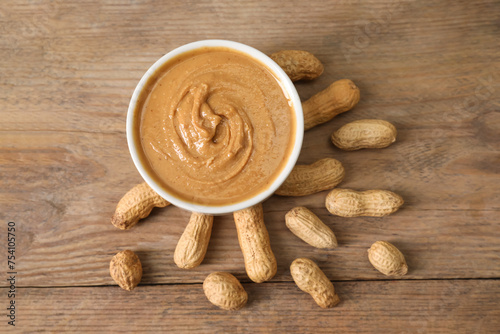 Delicious nut butter in bowl and peanuts on wooden table, top view