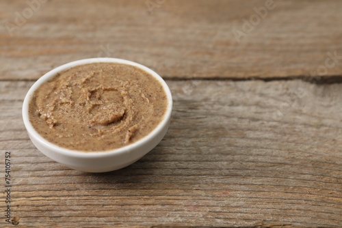 Delicious nut butter in bowl on wooden table, closeup. Space for text