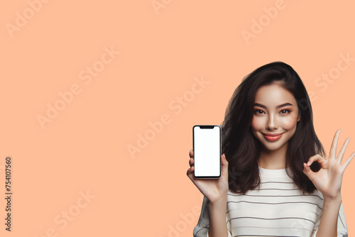 Beautiful Asian woman make an OK hand gesture  holding  mockup of blank screen peach Fuzz background 
