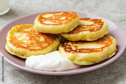 pancakes with sour cream. on a stone gray table there is a white plate with fried pancakes and sour cream, close-up, food concept