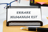 Latin quote Errare humanum est, meaning It is human nature to make mistakes. Mistakes are inherent in human existence. Text written on a business card on the table