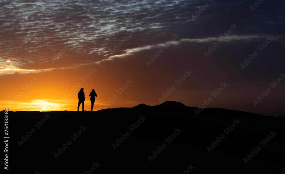 Silhouette of a couple running at sunrise on a dune in the desert of Morocco