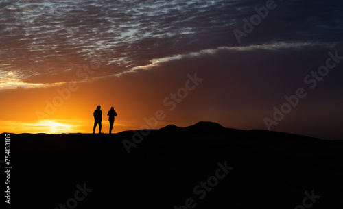 Silhouette of a couple running at sunrise on a dune in the desert of Morocco © stemue_photo