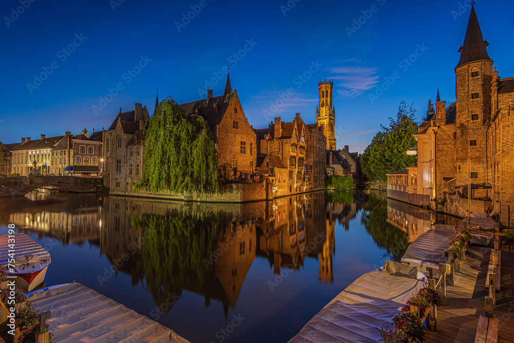 Center of the old town of Bruges with a view of the Rosary Quay. Old Belgian Hanseatic town with canal at blue hour. Reflections of illuminated historic merchant houses and belfry on the water surface