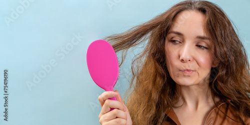 Woman holding pink hair brush, combing hair with intrigued face expression. Banner with copy space.