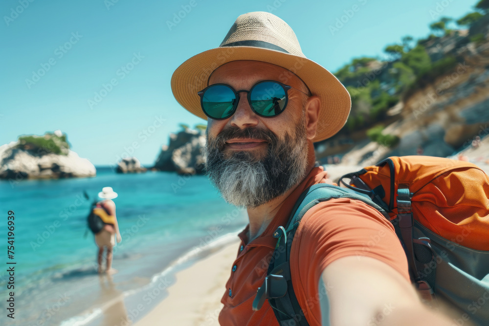 Man in hat with sunglasses on vacation with backpack on the beach selfie
