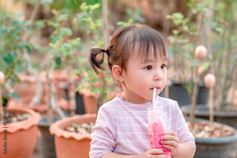 Little asian girl drink pink milk from a straw at park. Children healthy diet and nutrtion concept. Little asian girl drink pink milk from a straw at park. Children healthy diet and nutrtion concept.