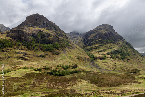 Clouds caress the peaks of the Three Sisters in Glen Coe, creating a dramatic and imposing highland landscape. Scotland