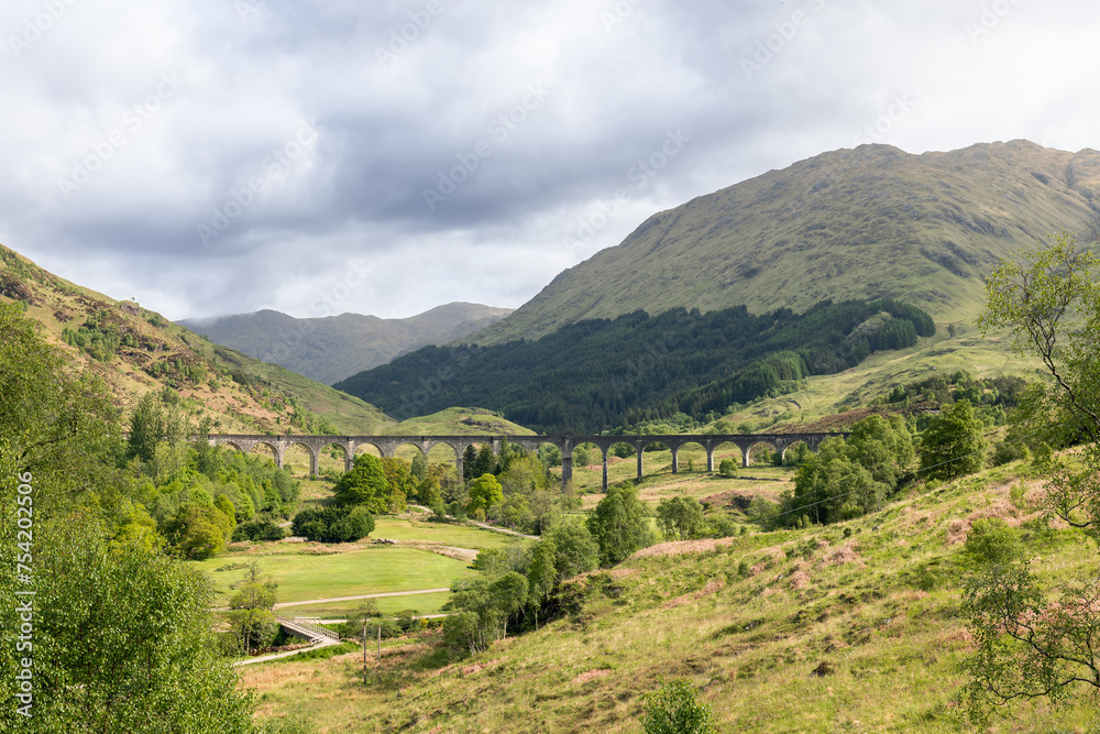 The Glenfinnan Viaduct arches gracefully over the lush Scottish countryside, embraced by rolling green hills