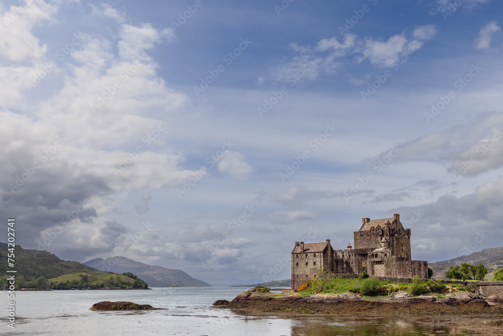 The storied Eilean Donan Castle presides over a peaceful loch, its image set against the lush greenery of the Highlands under a vast, expressive sky