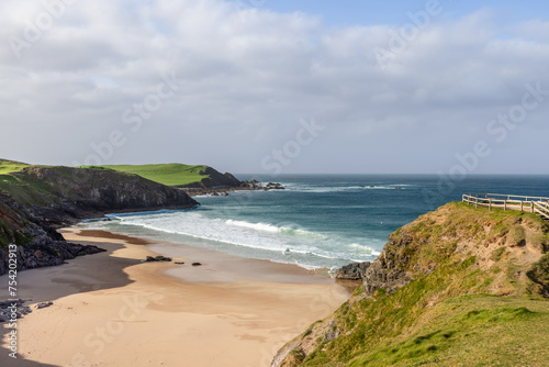 The tranquil beauty of Scotland's Durness Beach is captured in this image, featuring a secluded sandy bay bordered by emerald cliffs and the crystal-clear waters of the Atlantic