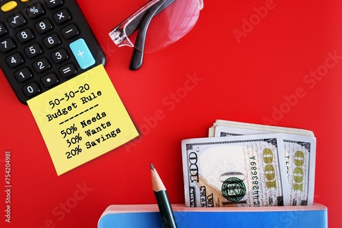 Dollars cash money calculator on red background with note written 50-30-20 budget rule, concept of recommend saving rule - putting 50% toward needs, 30% toward wants 20% toward savings photo