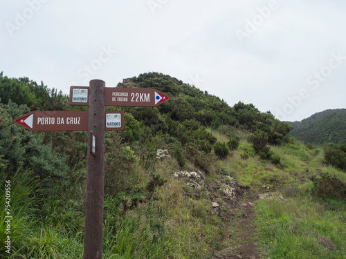 Green hills and meadow with footpath and tourist signpost pointing at Porto da Cruz in one direction and Percurso de treino at Machico in other. photo