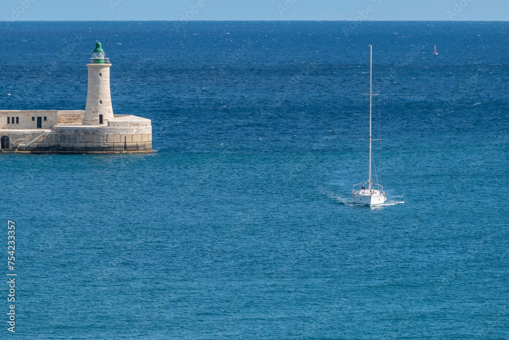 A boat enters the Grand Harbour of Valletta with the St. Elmo breakwater lighthouse in the background