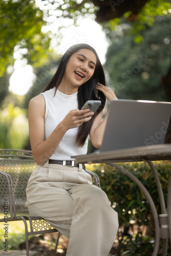 Young woman uses smartphone while working with laptop at outdoor cafe and coffee.
