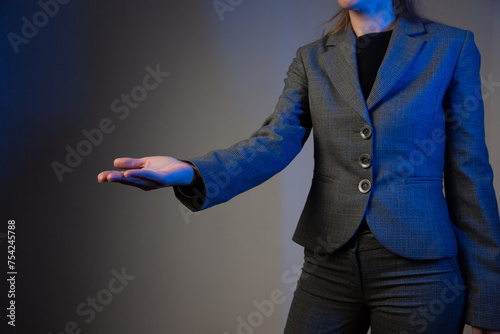 Part of a business woman with her arm extended forward and palm up. Gray background. Blue color correction. Side view