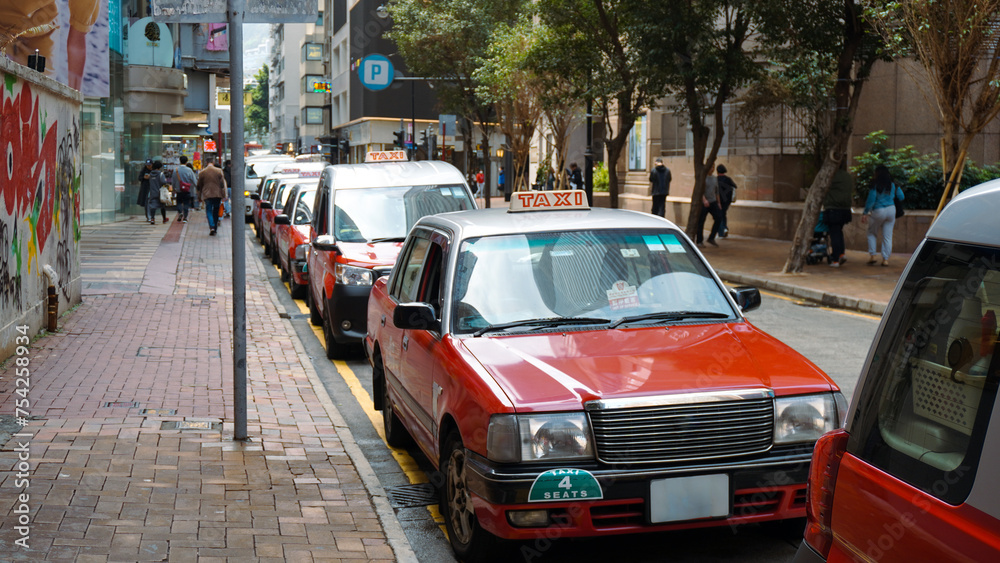 A fleet of Hong Kong taxis waiting at a taxi stand. Hong Kong taxis are easily recognizable by their red and white colors.