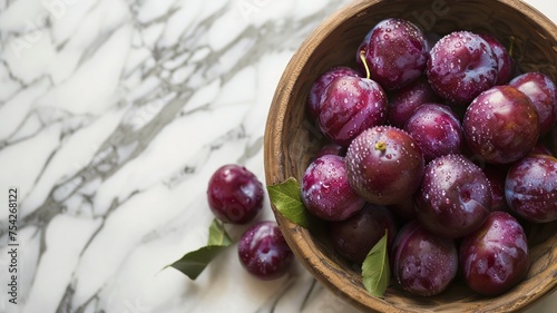 Fresh plums in a rustic clay bowl on a classic marble countertop