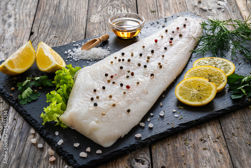 Tableau sur toile Fresh raw halibut fillet with lemon and dill on black stony  cutting board on wo