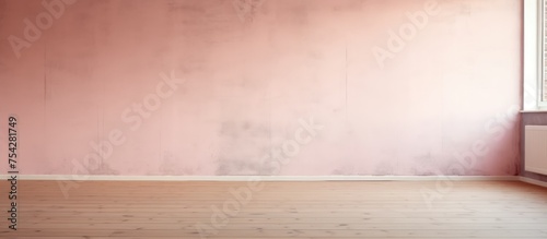 An interior view of an empty room featuring a radiator and a window. The room has a soft pink concrete wall and a wooden floor.