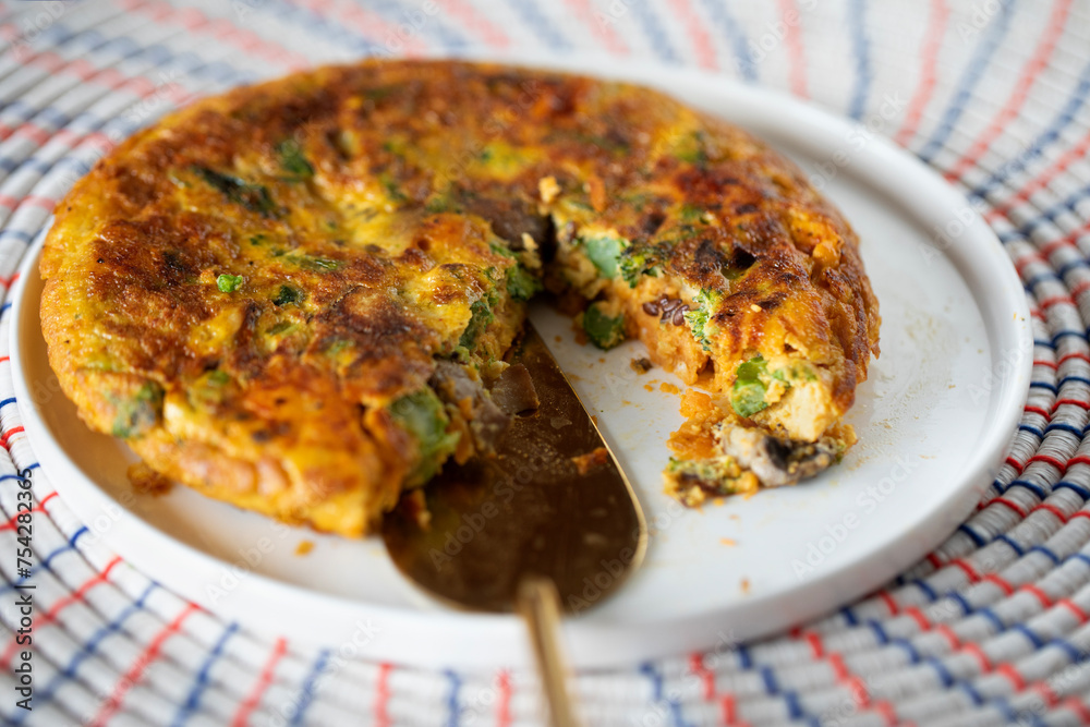 VEGETABLE FRITTATA CLOSE UP ON WHITE PLATE ON WOVEN AFRICAN MATT GOLD SERVING SLICE VEGETABLE FRITTATA CLOSE UP ON WHITE PLATE ON WOVEN AFRICAN MATT GOLD SERVING SLICE
