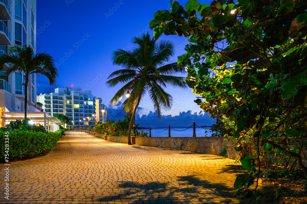 Fototapeta premium San Juan City Sunrise Landscape with tropical trees, buildings, and brick road along Pedestrian Shore Road around El Boquerón Bay and Balneario Condado Beach in Puerto Rico