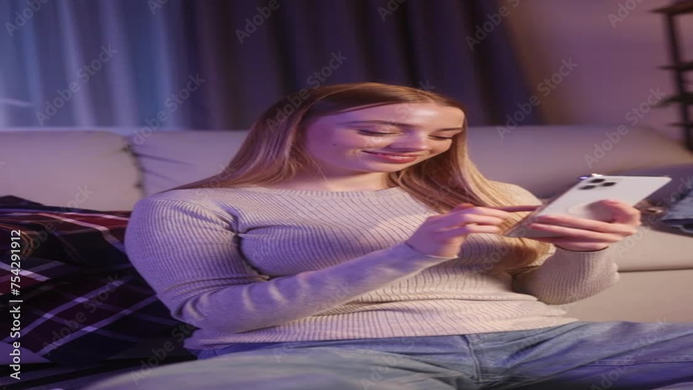 Vertical video of charming young blond woman hold smartphone scrolling app watching social media feed fashion app website or internet online store and sitting on clothes at wardrobe late at home Vertical video of charming young blond woman hold smartphone scrolling app watching social media feed fashion app website or internet online store and sitting on clothes at wardrobe late at home