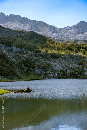 Lonely person admiring the lake of Covadonga reflection with mountains and nature, during sunny summer day in peaks of europe, spain