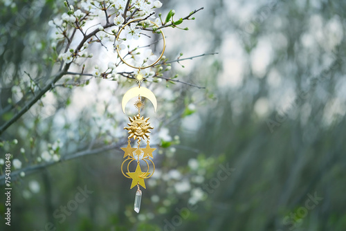 wiccan golden amulet with sun, moon, stars and crystal on blossoming cherry tree, natural abstract background. Sun symbol of spring equinox. witch ritual, spiritual esoteric practice. spring season