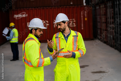 Two men in safety gear shake hands. One of them is holding a tablet. Scene is professional and friendly