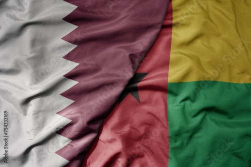 big waving national colorful flag of guinea bissau and national flag of qatar.