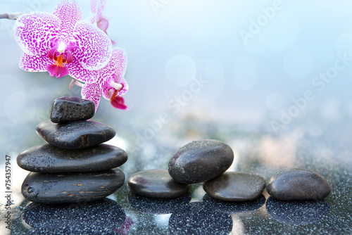 Black spa stone and pink orchid flowers on the gray table background.