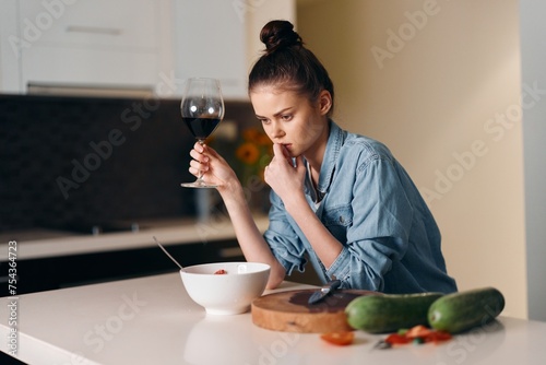 Solitary Reflection: A Sad, Beautiful Woman Sitting Alone at Home, Holding a Glass of Wine on a White Kitchen Table.