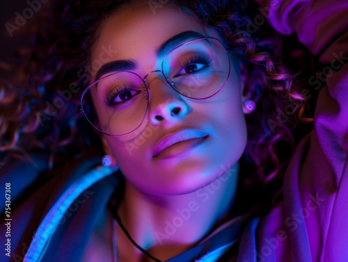 A multiracial woman is wearing glasses while being illuminated by a blue light