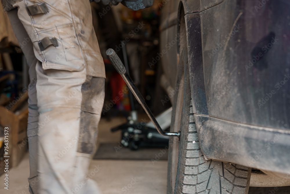 A mechanic repairs a car chassis. A man removes car wheels using a pneumatic screwdriver A mechanic repairs a car chassis. A man removes car wheels using a pneumatic screwdriver