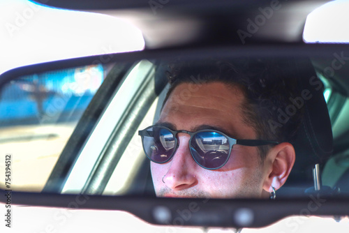 Caucasian man with sunglasses reflected in car rear-view mirror while driving on the road