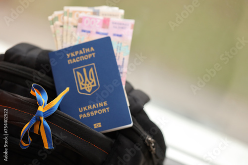 Ukrainian biometrical passport and UAH money bills on touristic backpack close up