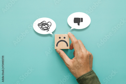 Service rating, satisfaction and negative feedback concept. Customer show bad face emoticon on a wooden cube with a unlike thumb down and confusion symbol in a speech bubble