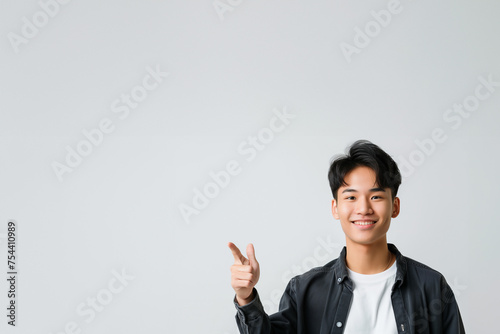 jeune homme asiatique, aux cheveux courts habillé d'un t-shirt blanc et d'une surchemise noire, qui pointe du doigt vers l'autre bout de l'image, sur fond clair avec espace négatif copyspace