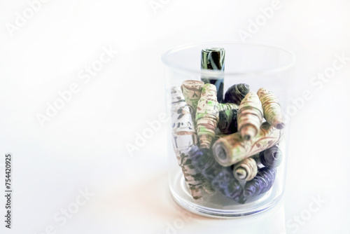 Handmade paper beads of brown, green, black colored floral patterns in plastic glass on white table side view