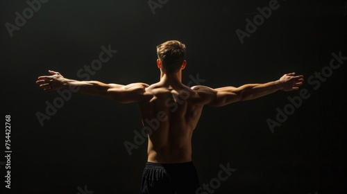 Rear view of healthy muscular young man with his arms stretched out isolated on black background © Sasint