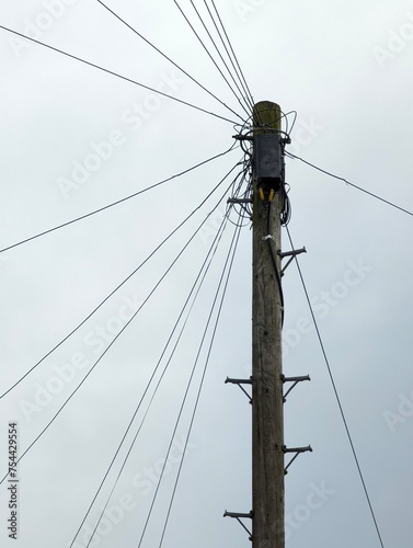 Wooden telegraph pole against a bleak featureless sky with cables routeing off in all directions connecting homes and businesses. Soon to be made obsolete and replaced by internet connections.