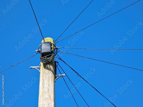 Wooden telegraph pole against a blue sky with cables routeing off in all directions connecting homes and businesses. Soon to be made obsolete and replaced by internet connections.